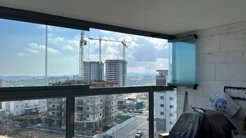 תמונה של מרפסת סגורה על חלון זכוכית שקוף שרואים נוף עירוני ברקע